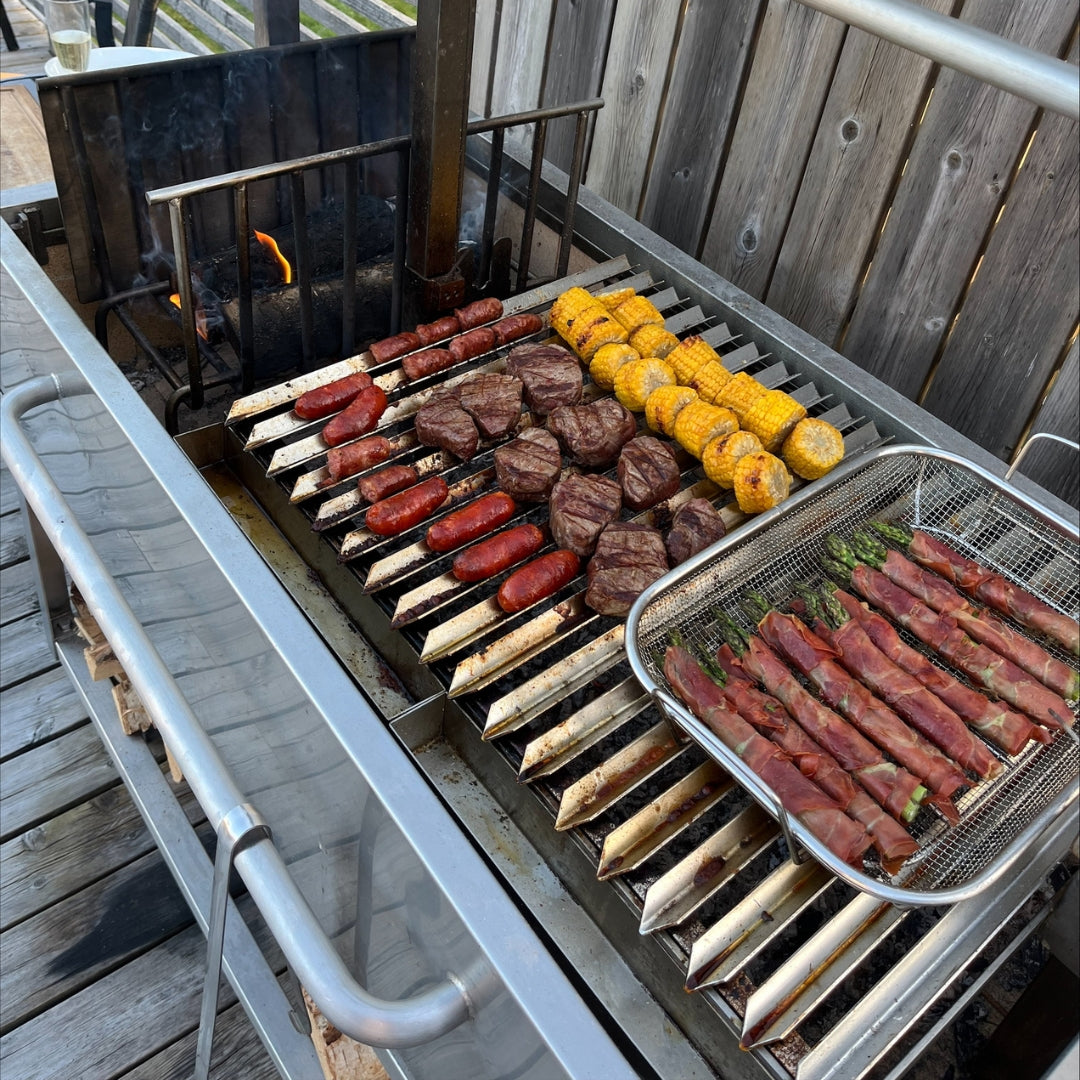 Argentinisches Asado-Festmahl mit Chorizo, Rindfleischpasteten, Mais und mit Prosciutto umwickelten Spargel auf Omberg Asado Grillrosten