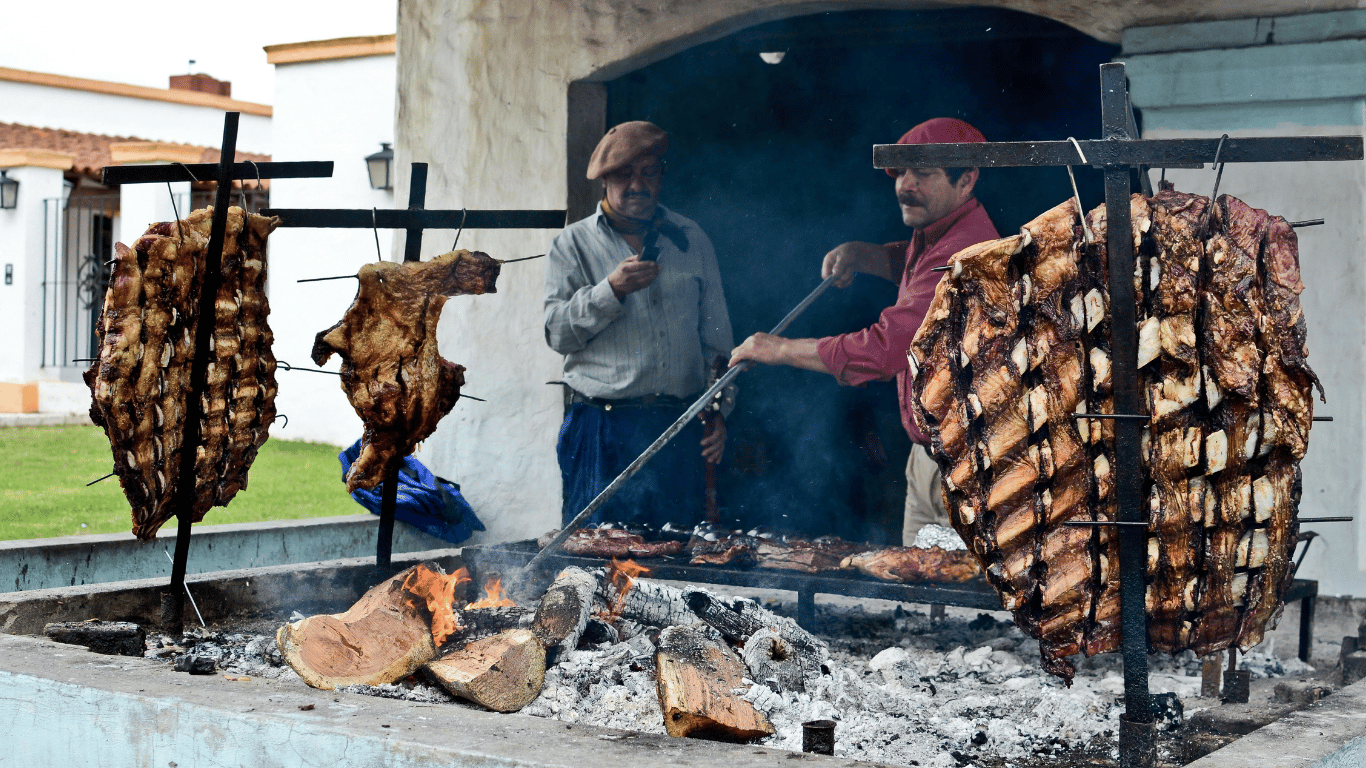 Two asadors managing whole cuts of meat on traditional Argentine vertical parrilla grill