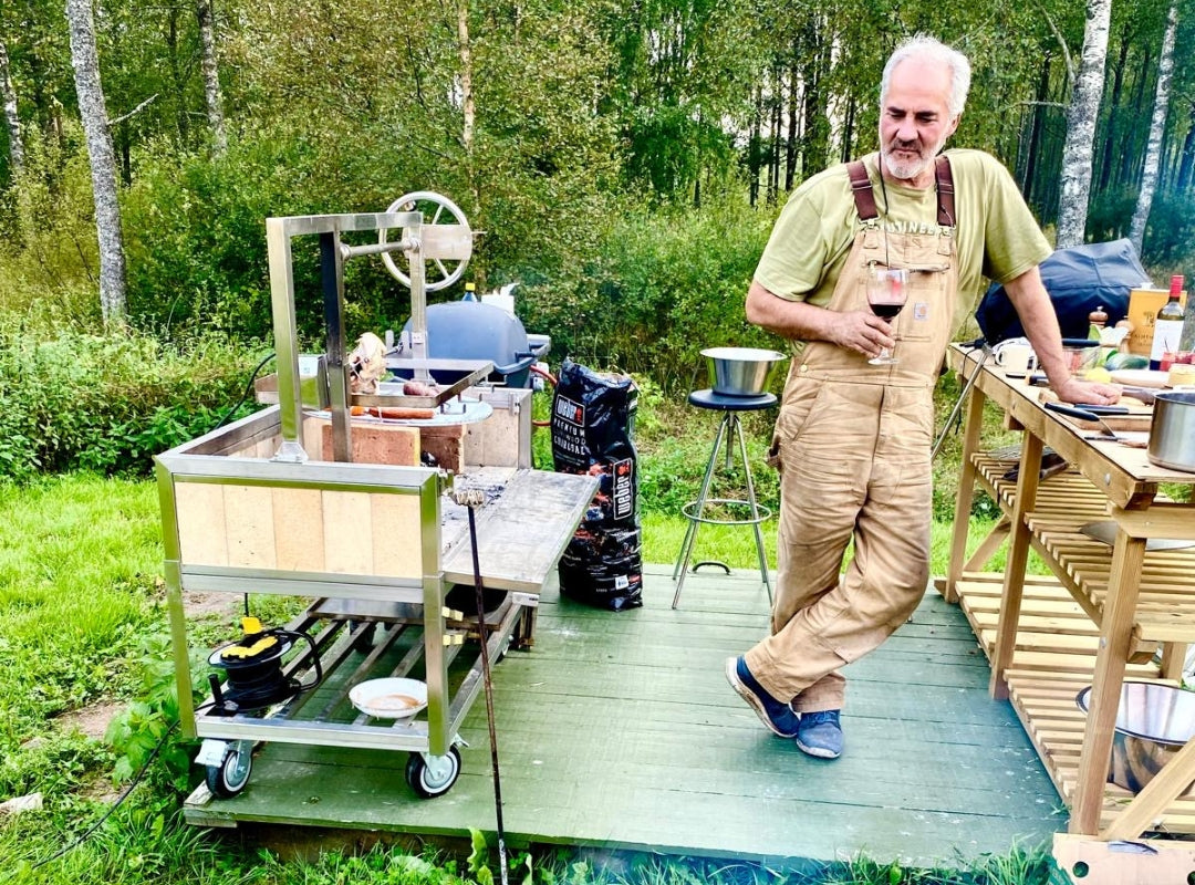 Image of one of our many satiesfied customers cooking dinner on his Omberg Asado Gaucho 1200, holding a glass of wine in the process
